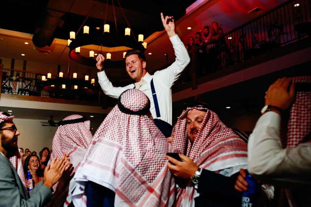 Groom lifted on shoulders during a Dabke dance celebration at an Arab wedding reception, groomsmen wearing traditional keffiyeh headscarves, St. Louis wedding photography