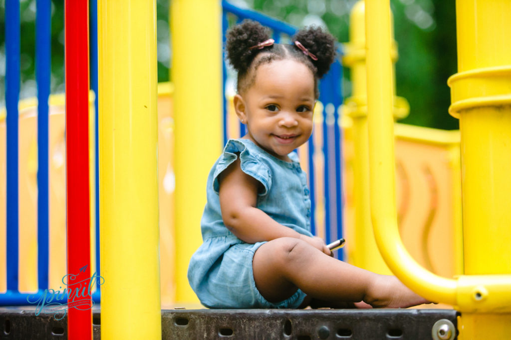 Adorable little girl in denim jumper sitting on playground equipment - shes smiling 
