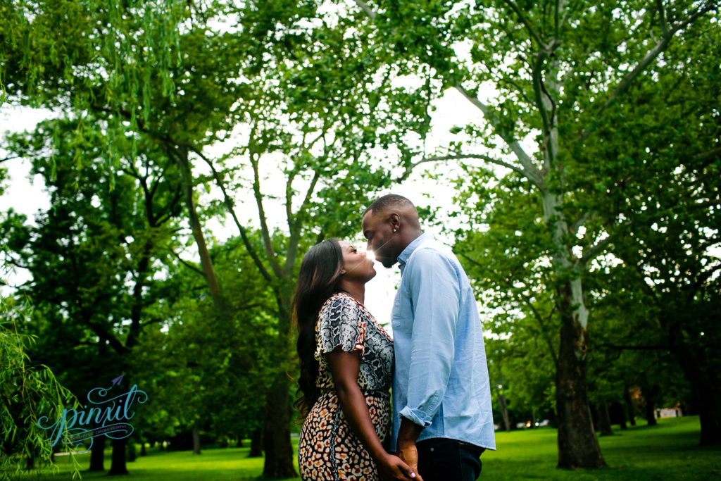 couple going in for a kiss with a little sunflare peeking though between their lips during their engagement session in tower grove park St Louis Mo 