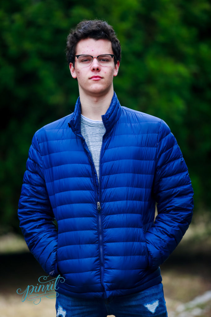 St Louis high school senior wearing glasses and blue puffy coat standing in tower grove park 