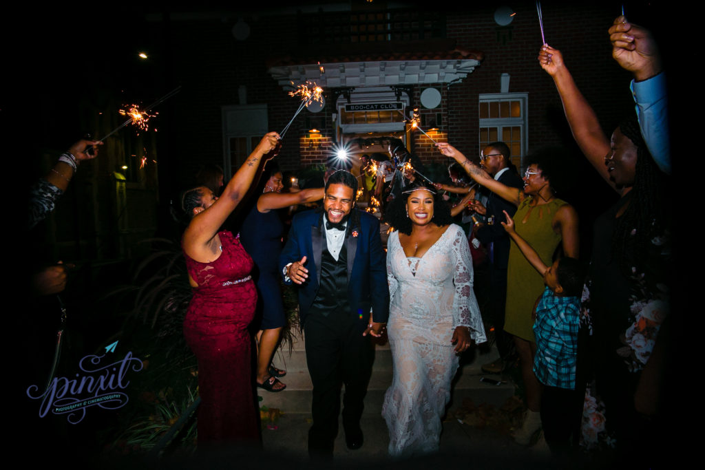 Couple running smiling through their friends and family holding sparklers out of their wedding venue, Boo Cat Club in St Louis MO