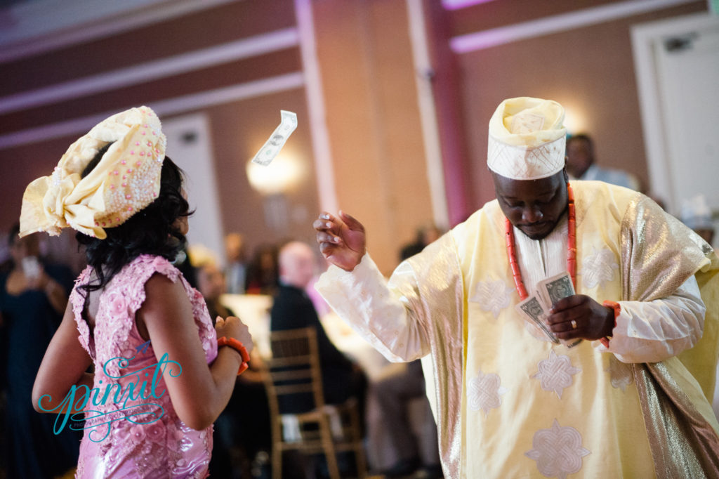 Groom showering his bride with money during their Nigerian wedding ceremony and reception. They are both wearing beautiful bright colors 