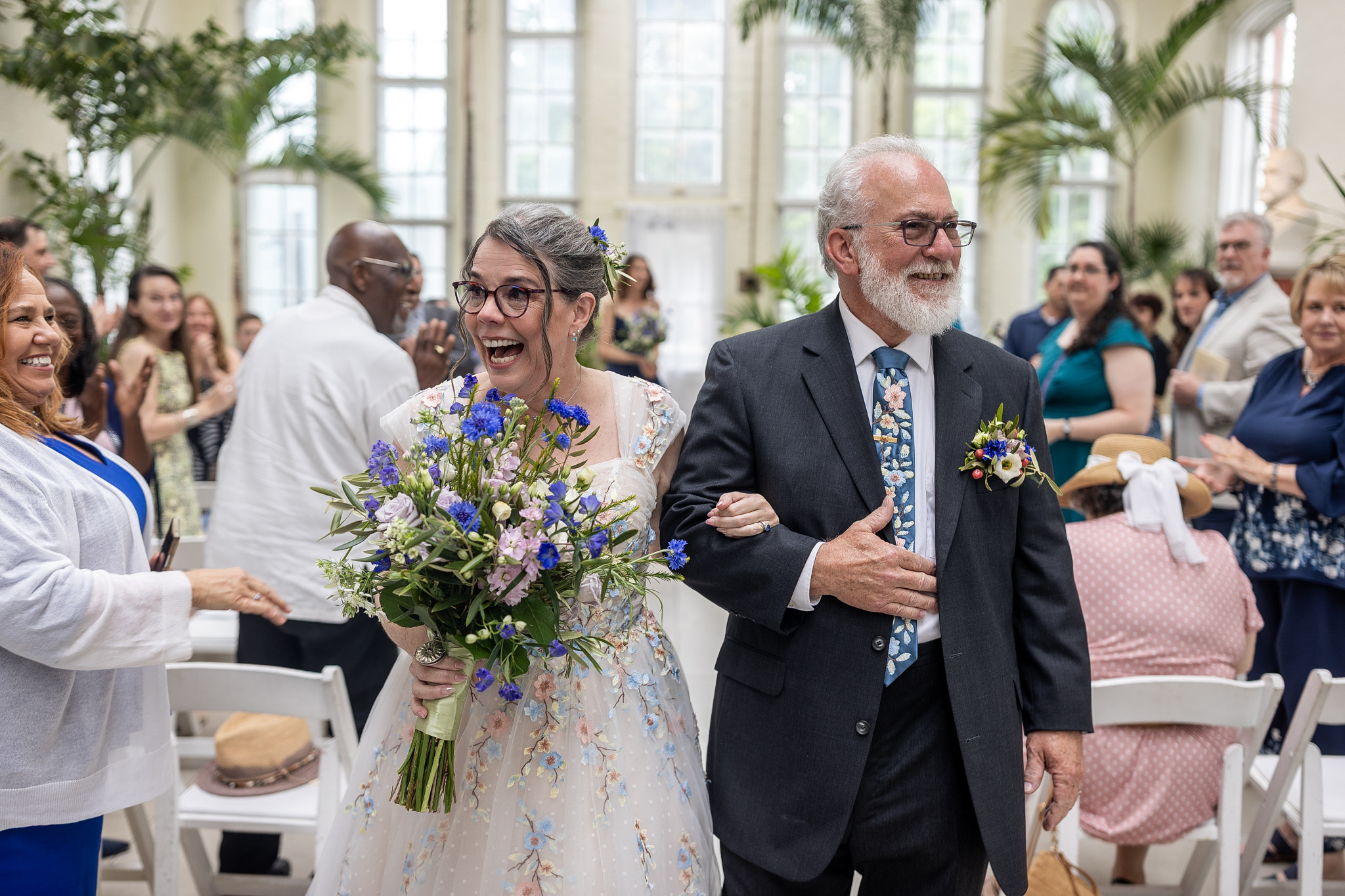 Mature couple exits their wedding ceremony at piper palm house with joy - thebride is carrying flowers nd the groom is smiling broadly